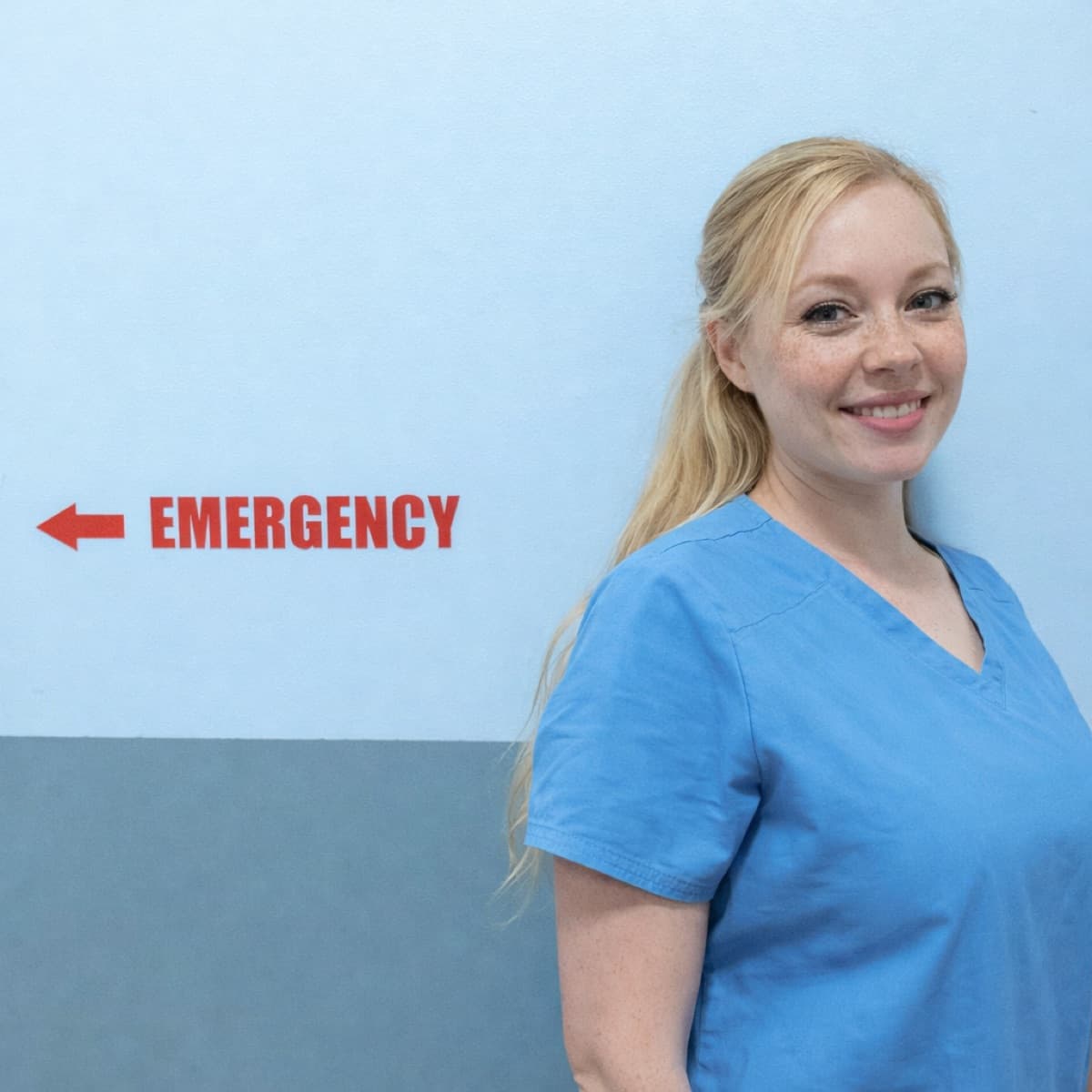 Healthcare professional in scrubs standing in a clinical corridor.